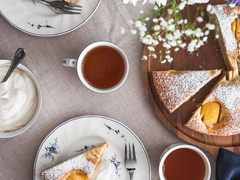 Old Luxembourg crockery with slices of cake with whipped cream, tea and flowers on a table.