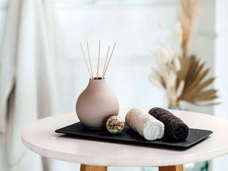 Beige Manufacture vase with fragrance sticks on a tray with towels.