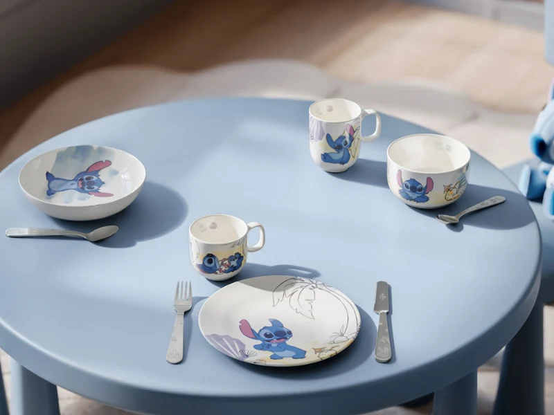 Una mesa azul con platos, cuencos y tazas de Disney Stitch al estilo de los dibujos animados. Una mesa azul con platos, cuencos y tazas de Disney Stitch de estilo cartoon, así como tenedores y cuchillos para dos personas.