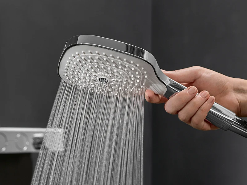 Une main tient une douchette d'où jaillit l'eau dans une salle de bains moderne.