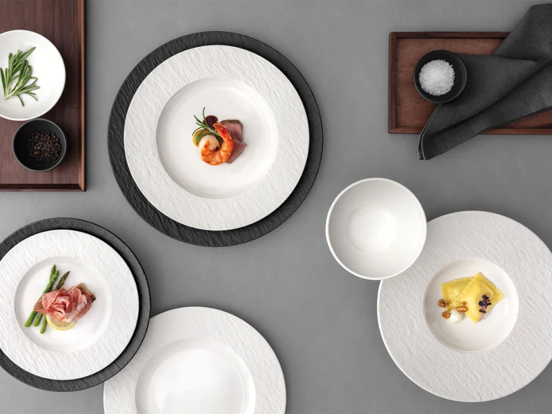 A formal table setting with Manufacture plates A formal table setting with a white and black plates, with food on it on a grey table.