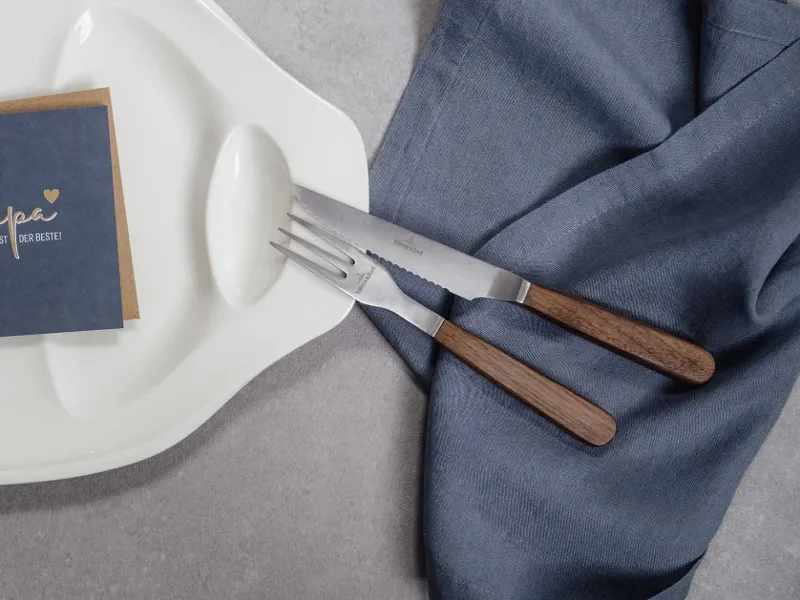 Elegant table decoration with modern wooden-handled Texas cutlery and a menu card on a textured linen napkin.