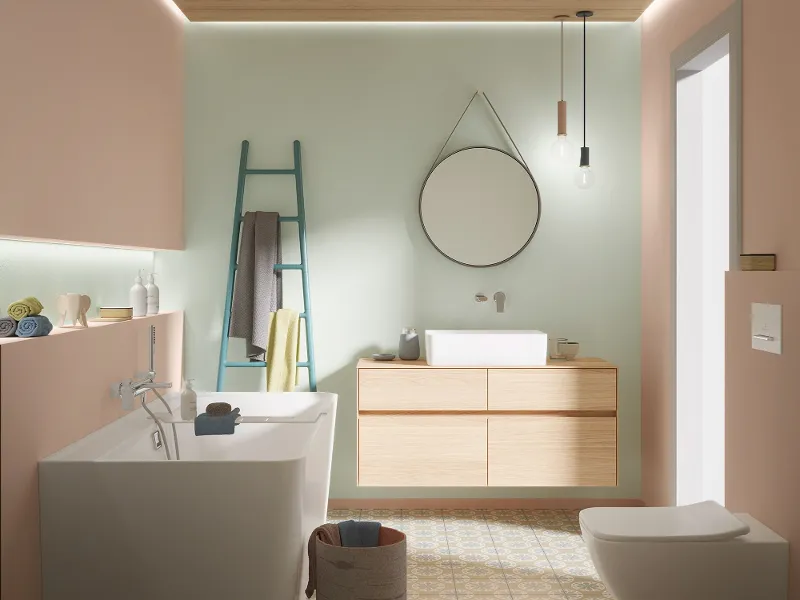 Modernes Badezimmer mit Wänden in Pastellrosa und Mintgrün, ausgestattet mit einer Badewanne, einem Waschbecken mit Holzschrank, einem Leiterregal, einem runden Spiegel, Hängelampen und einer Toilette.
