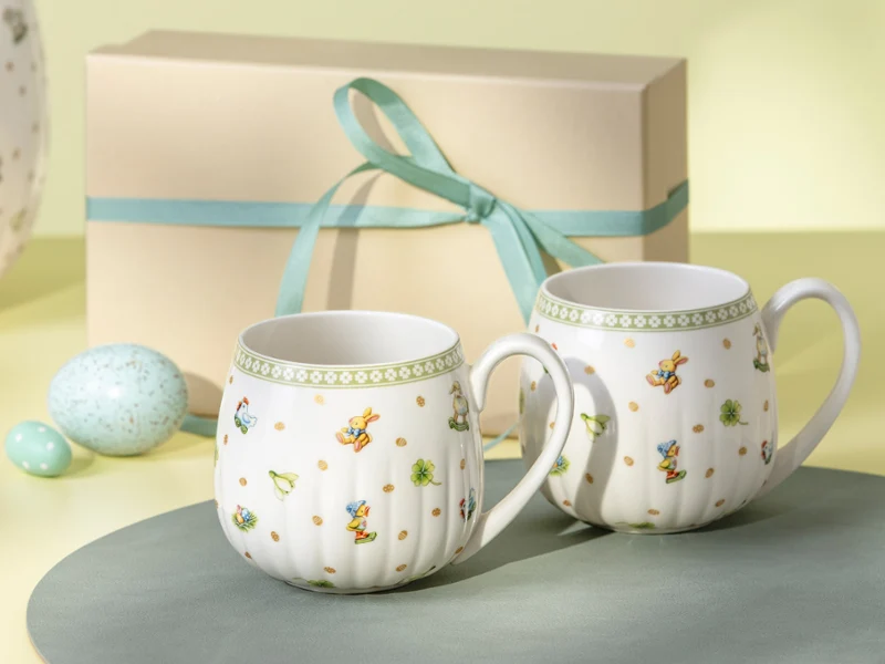 Two Easter Delight mugs with floral patterns are placed in front of a gift box tied with a light blue ribbon.