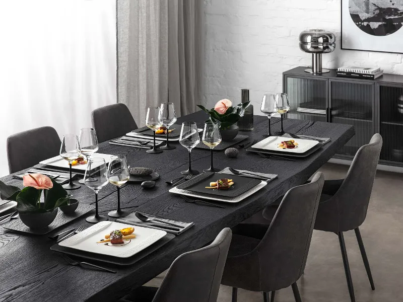 A black table in an elegant living room set with glasses, rectangular crockery and cutlery from the Villeroy & Boch Manufacture collection.