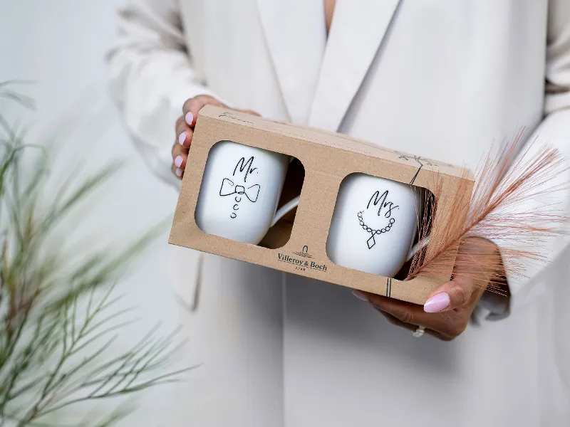 A person holding a gift box containing two Statement cups with the words "Mr" and "Mrs".