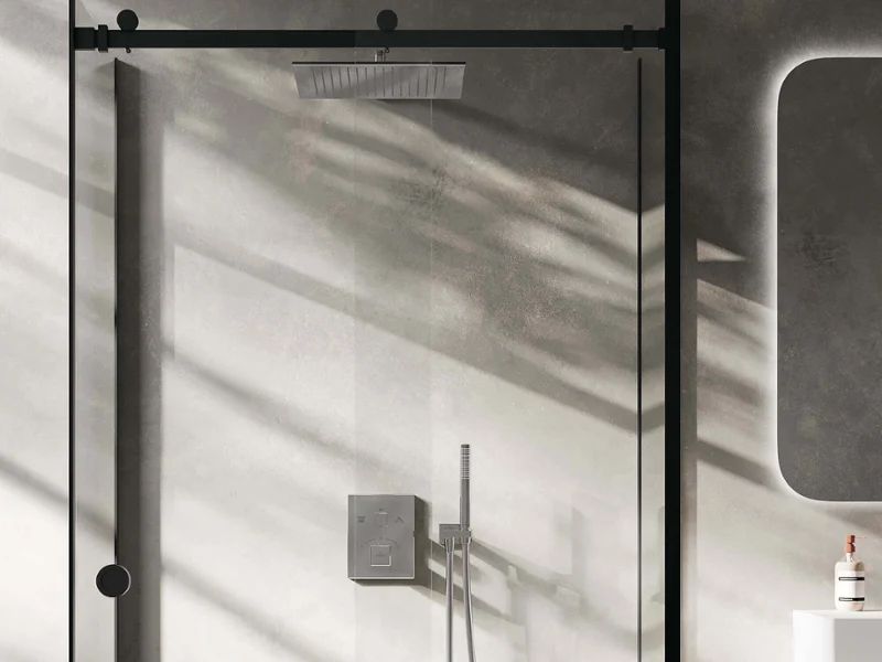 Universal Showers shower fitting in a bathroom with a Squaro Infinity shower tray Modern glass shower enclosure with a black frame and wall-mounted shower control, illuminated by natural light.