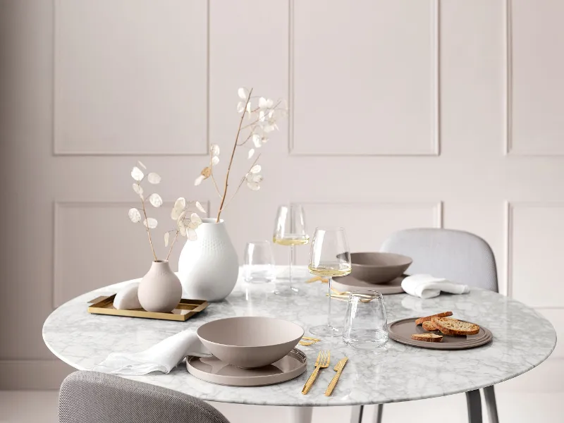 A dining table with a white table cloth and a vase of flowers, set with La Boule Pure Beige and MetroChic wine glasses.