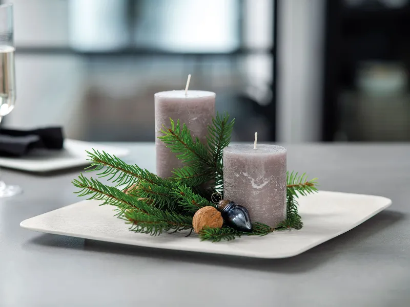 Two grey candles, surrounded by sprigs of fir and nuts, on a white Manufacture plate.