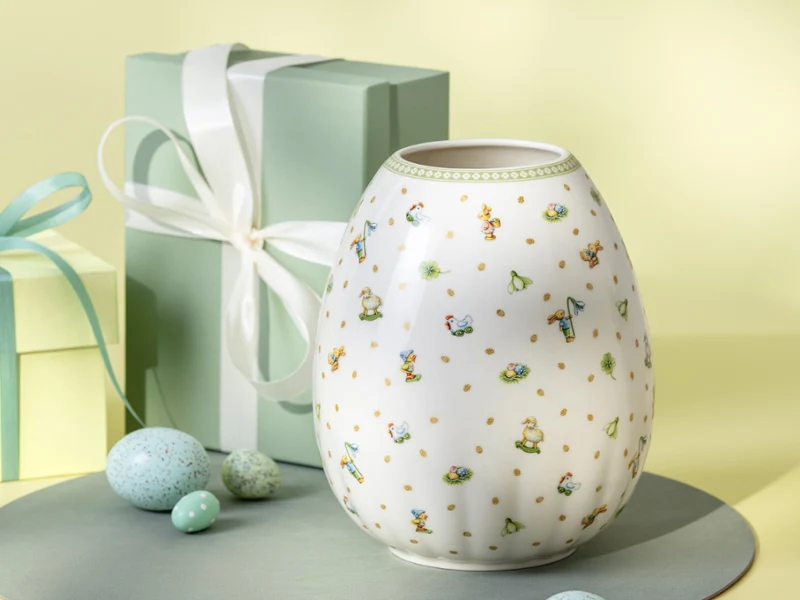 A white Easter Delight vase with floral designs A white Easter Delight vase with floral designs is displayed beside two pastel gift boxes and speckled eggs.