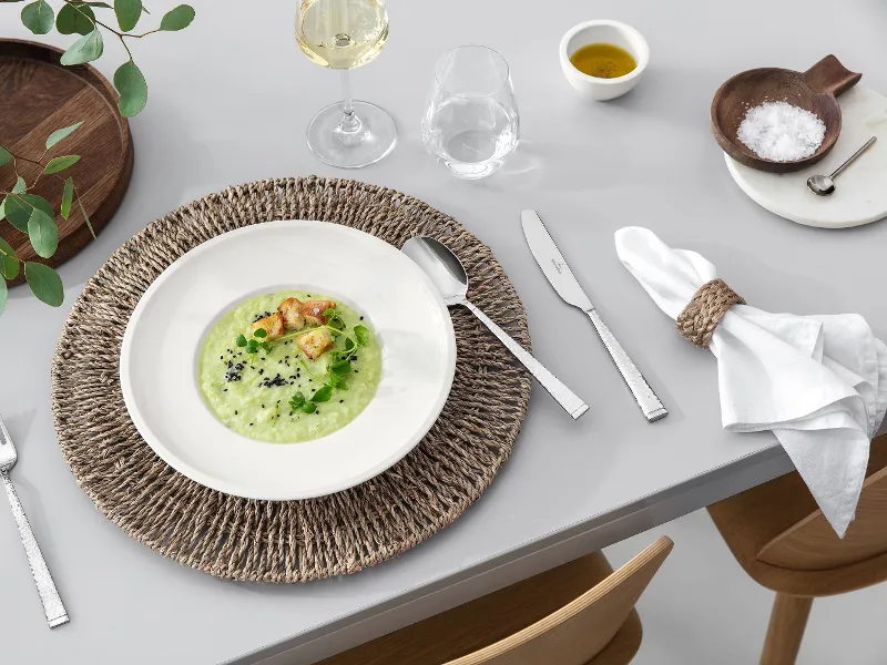 A dining table with Blacksmith cutlery, an Artesano plate filled with soup, a glass of white wine and rustic table decoration.