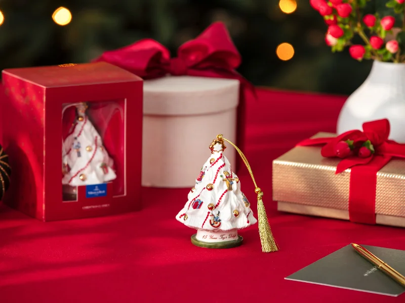 Porcelain Christmas tree ornaments on a red table, near a gift box, packaging, and a pen with Christmas decorations.