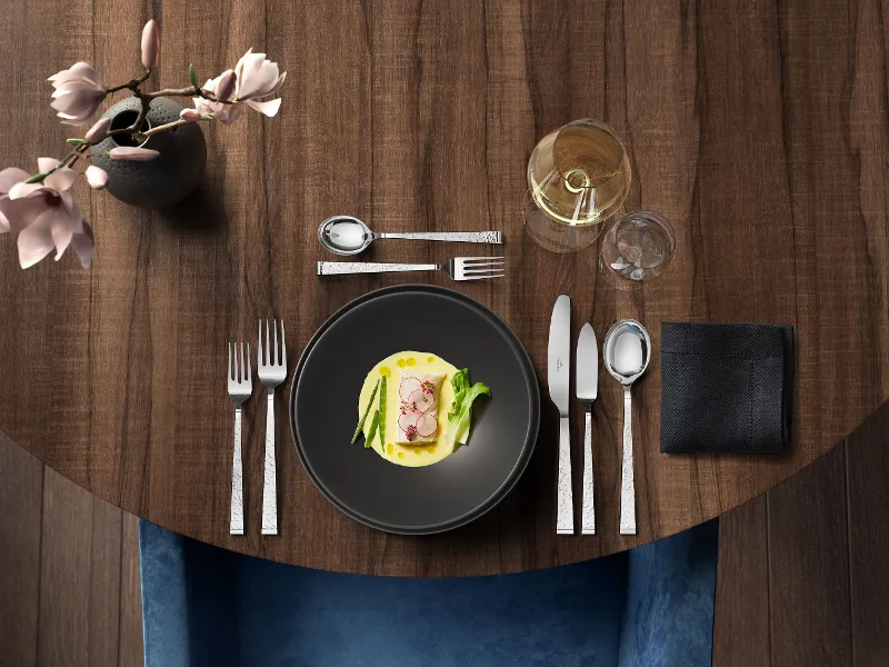 Elegantly laid dark round table with a starter accompanied by a glass of white wine and the Blacksmith cutlery set.