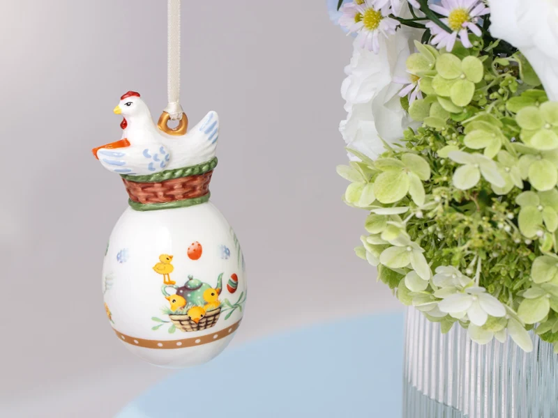Ceramic Annual Easter Edition 2026 ornament with a chicken design hanging near a bouquet of green and white flowers in a vase.