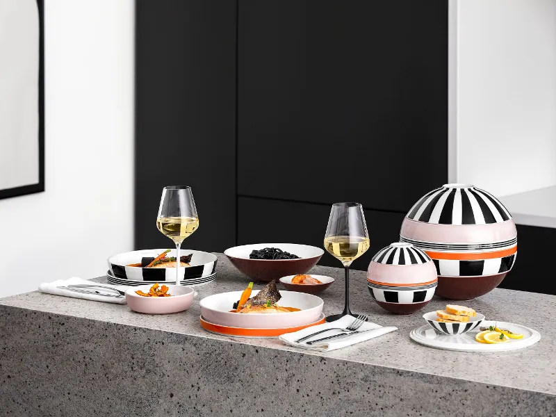 Un tavolo moderno con La Boule e La petite Boule a fantasia, bicchieri da vino e snack su un piano di lavoro grigio in una cucina minimalista.