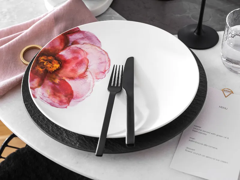 Table decoration with a Rose Garden plate with a floral decor on a black Manufacture plate along with black cutlery and a menu.