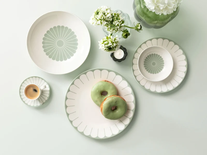 Plate with a green and white pattern on a light green surface with two green donuts and a small bouquet of white flowers.	