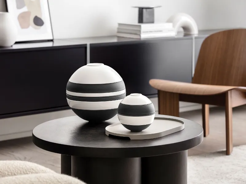 Un soggiorno moderno con La Boule di Villeroy & Boch in bianco e nero accanto a La petite Boule in bianco e nero su un tavolo rotondo scuro. 