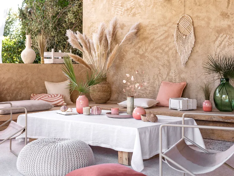 Boho-style outdoor seating area with wooden benches, cushions, a placemat for tea, plants and decorative vases.