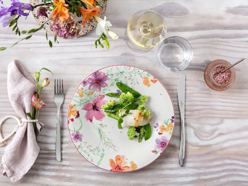 Elegant dining table with a floral-patterned Mariefleur plate, a healthy meal and a glass of white wine.