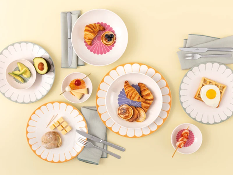 Table setting with Villeroy & Boch Fleur Soleil plates, eggs, tea with a slice of lemon, and white flowers on a light yellow background.