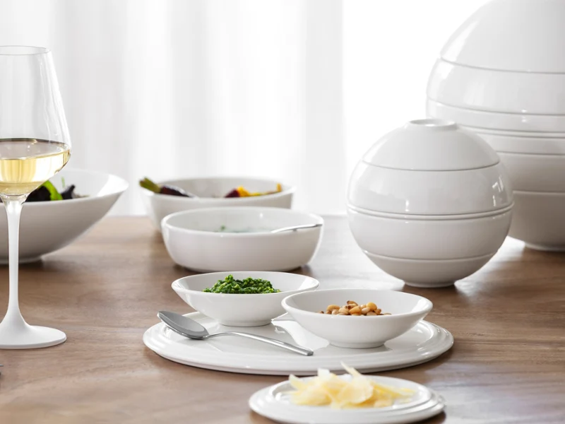 La Boule & La petite Boule in bright white A white wine glass and white ceramic dishes with food are arranged on a wooden table with soft daylight.