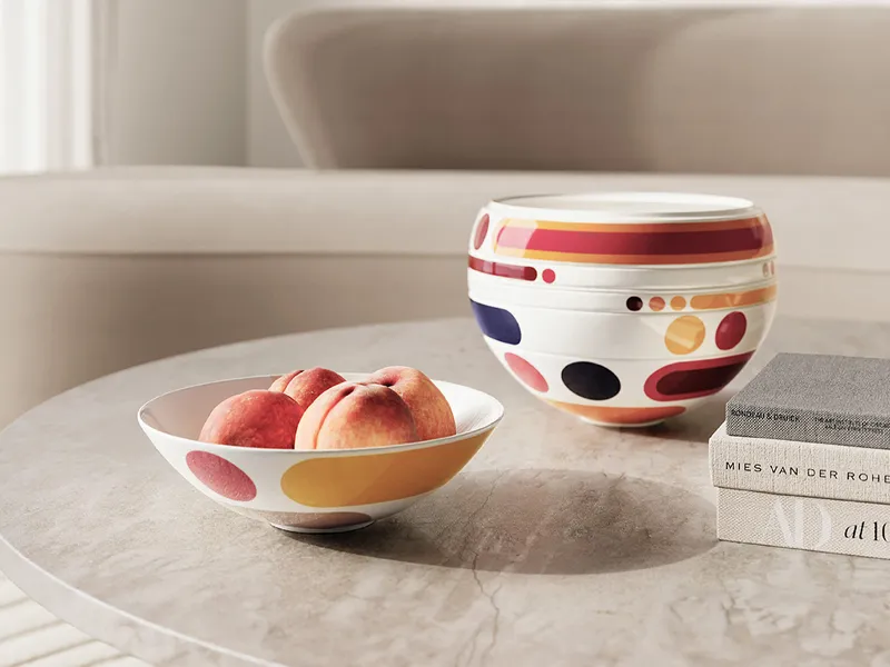 A La Boule Miami bowl with peaches and a decorative bowl with colorful patterns on a marble table next to stacked books in a bright, modern living room.