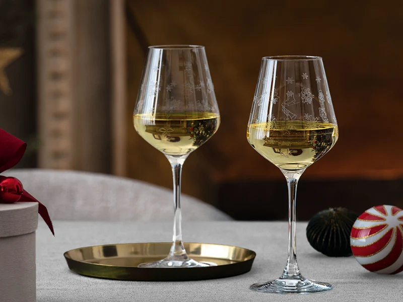 Two glasses of white wine on a set table Two glasses of white wine on a set table with a gift box, Christmas decorations, and a brass tray in the background.