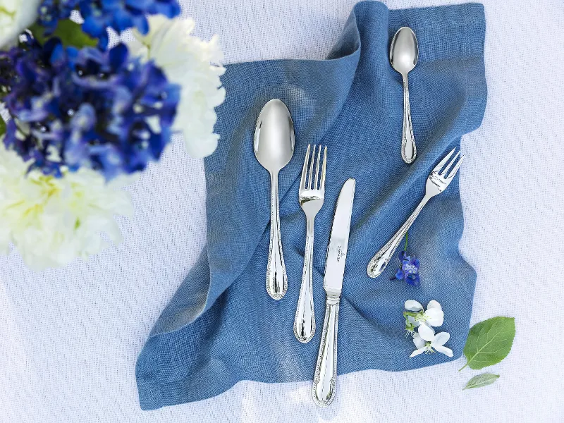 Stylish table decoration with Mademoiselle cutlery on a blue linen napkin and a bouquet of flowers.