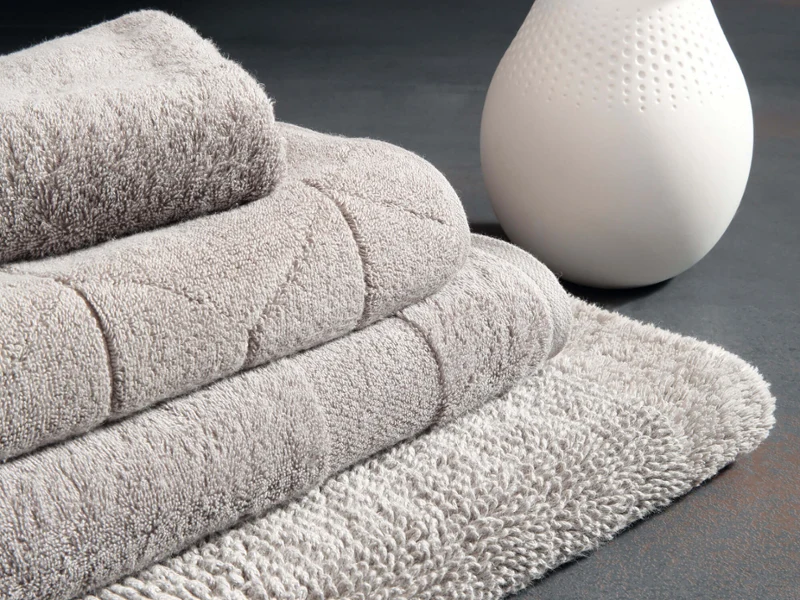 Elegancka dekoracja łazienki z ręcznikami One i wazonem Manufacture Collier marki Villeroy & Boch Zestaw różowych ręczników z kolekcji "One" marki Villeroy & Boch,
w tym jeden ze wzorem liści z kolekcji Leaf wisi nad białą wanną z ciemną ścianą w tle.