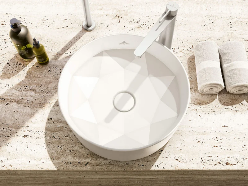 Round white washbasin on a speckled countertop with a faucet, towels, and a soap dispenser nearby.