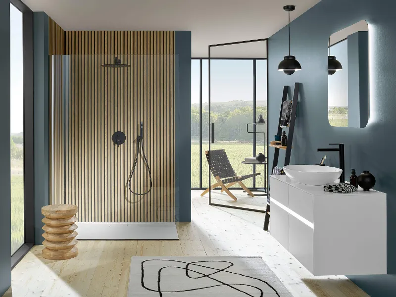 Black Universal Showers shower tap in a petrol-coloured bathroom with large windows and a washstand.