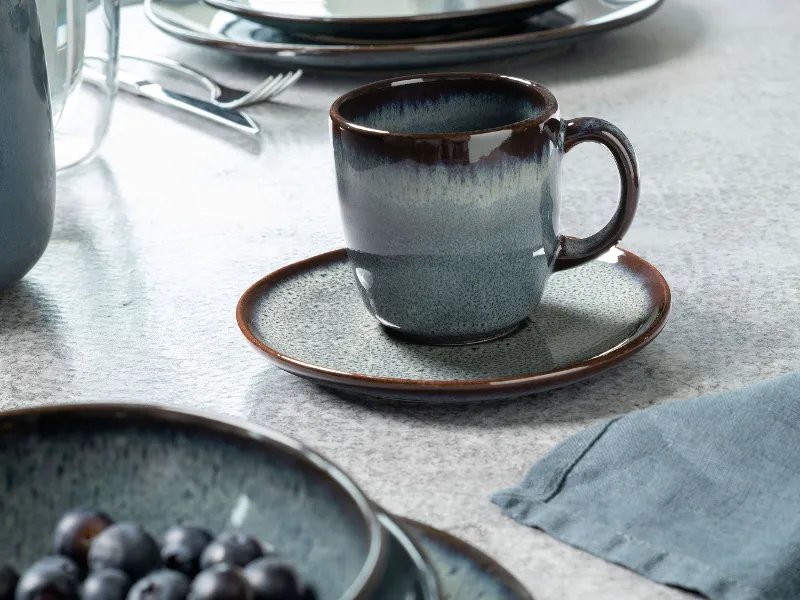 Lave cup on a matching saucer, surrounded by similar crockery and a bowl of blueberries.	