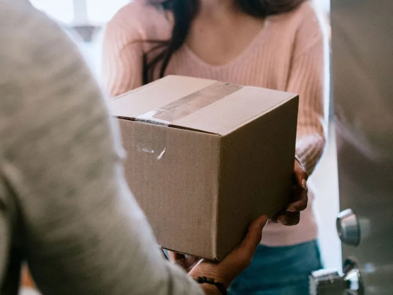 A person hands a box to another person in a doorway.