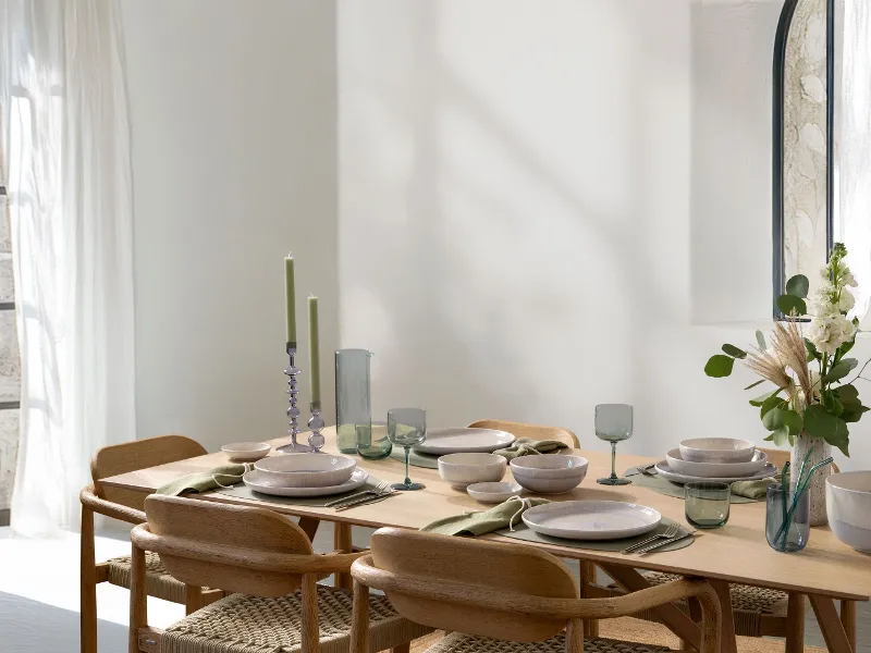 Modern dining table setting with Villeroy & Boch like ice glassware, perlemor sand porcelain, wooden chairs and natural decoration in bright room with open windows
