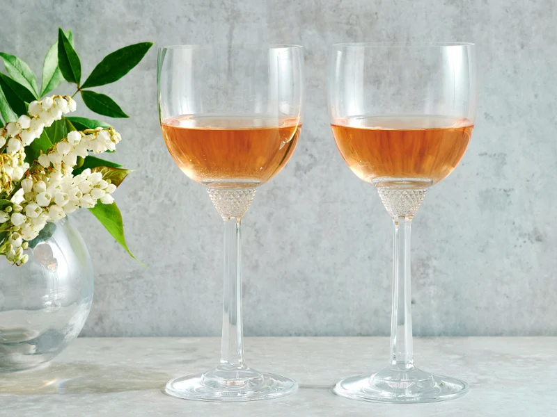 The Octavie Wine Gift Set, featuring two crystal glasses filled with rose champagne, complemented by a vase of florals.