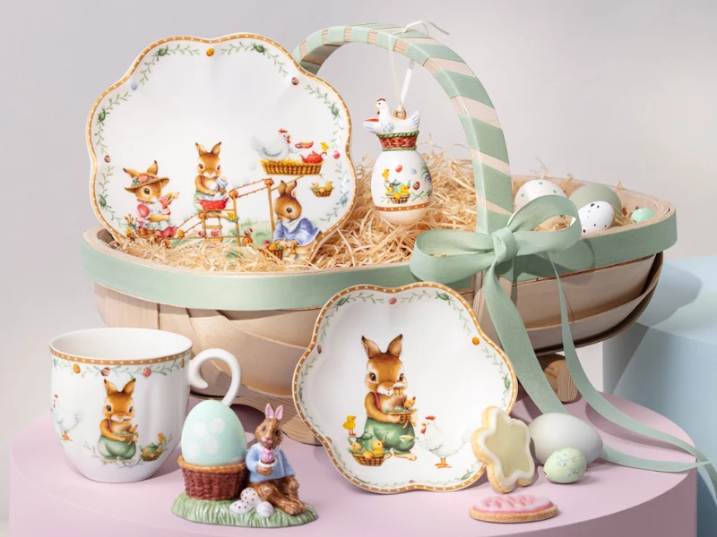 A decorative Annual Easter Edition 2026 basket with bunny-themed plates, cup, figurine, cookies, eggs, and a green ribbon.