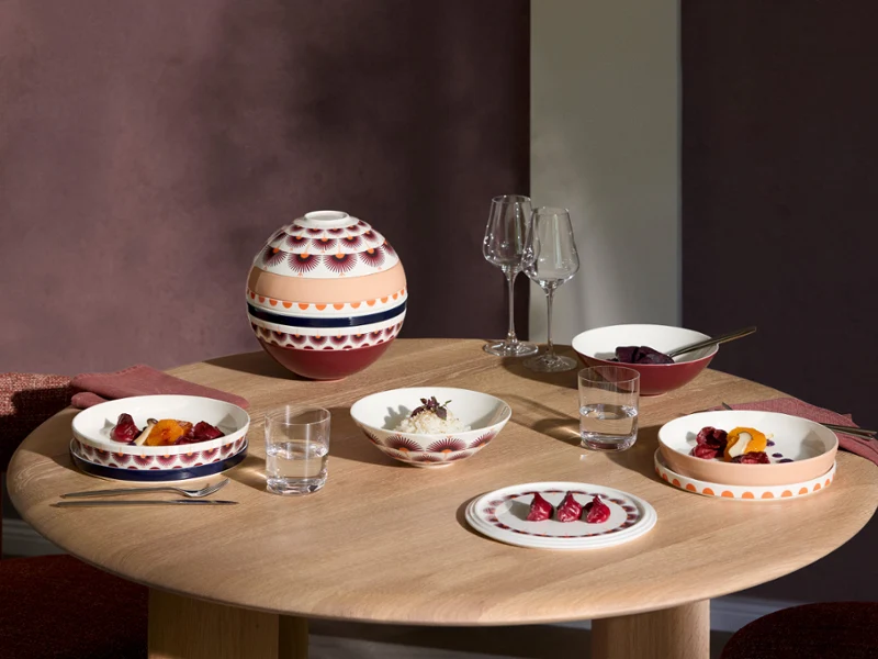 La Boule Kyoto tablesetting with food A round wooden table set with patterned tableware from La Boule Kyoto, glasses, and a bowl with a lid, ready for a meal for three.