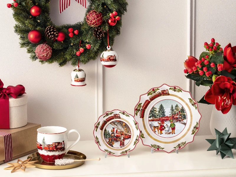 A decorated Christmas wreath hangs above a table with festively set plates, a cup, and a poinsettia arrangement. 