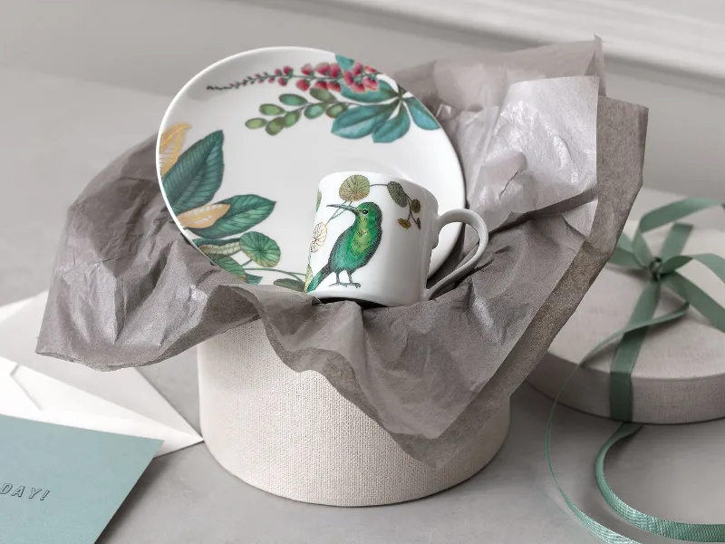 Eine Villeroy & Boch Avarua-Teller und Tasse vor einer Geschenkbox, präsentiert mit einem Umschlag und Boxdeckel.