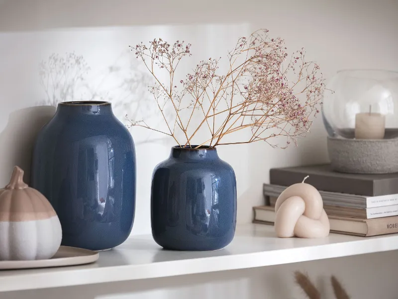 Two blue Lave vases standing on a shelf next to a decorative porcelain pumpkin.