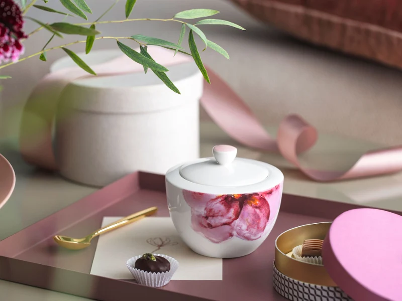 Rose Graden Zuckerdose mit goldenem Löffel auf einem Tablett Eine Rose Garden Zuckerdose mit einer Kerze, einem goldenen Löffel, einem Schokoladentrüffel und Dekorationsgegenständen auf einem Tablett.