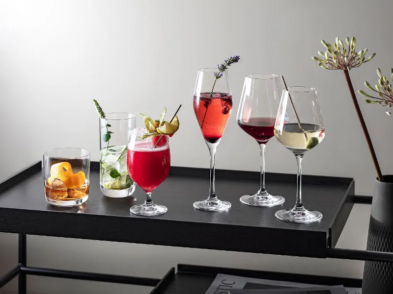 Various drinks in La Divina glasses presented on a modern black tray, decorated with herbs and fruit.