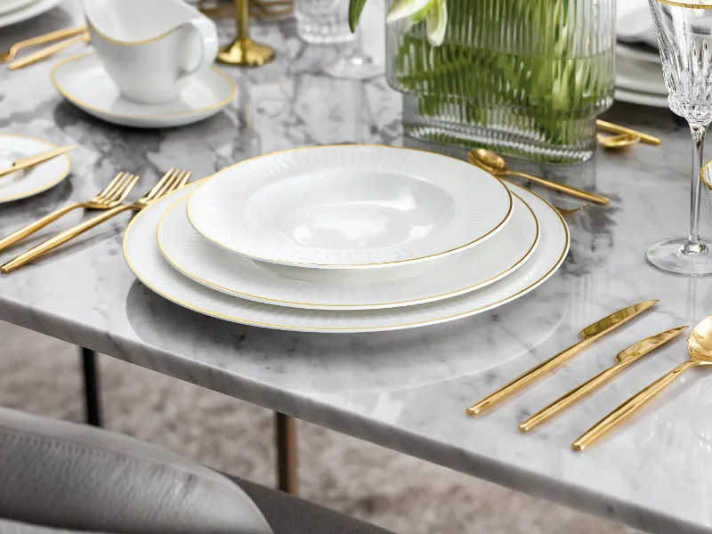 Elegant table decoration with white Château Septfontaines plates, gold MetroChic d'Or cutlery and crystal glasses on a marble table.