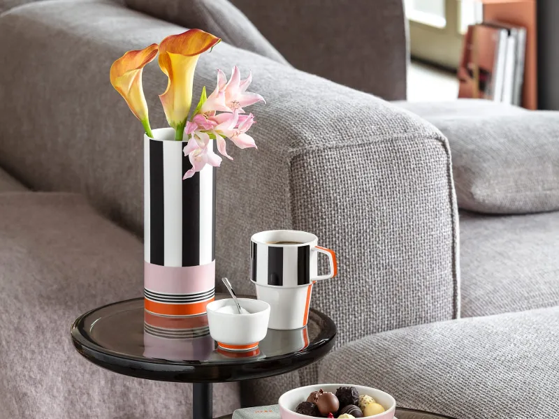 Zwei runde Beistelltische mit einer Memphis-Blumenvase, einer Memphis-Kaffeetasse, einer Zuckerdose, einem Buch und einer Schale Pralinen in einem modernen Wohnzimmer.