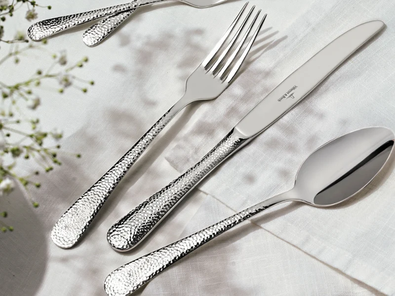 A polished silverware set displayed on a white tablecloth, featuring forks, knives, and spoons arranged neatly.