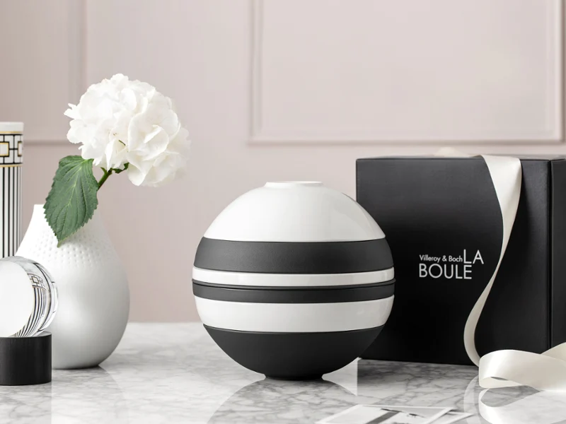 A Villeroy & Boch black and white La Boule on a marble surface. A Villeroy & Boch black and white La Boule on a marble surface, accompanied by a white vase with a flower and an open black box labelled "La Boule".