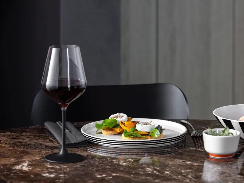 Ein Esszimmer mit einem Glas Rotwein, Memphis Tellern mit Vorspeisen und zwei Memphis Schüsseln auf einem Marmortisch.

