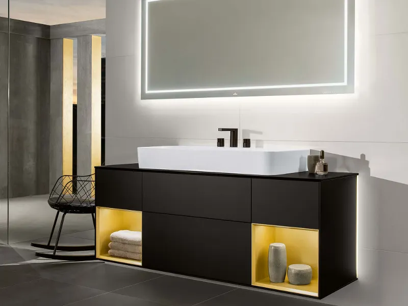 A Finion washbasin with an illuminated vanity unit and illuminated mirror in a dark-coloured bathroom.