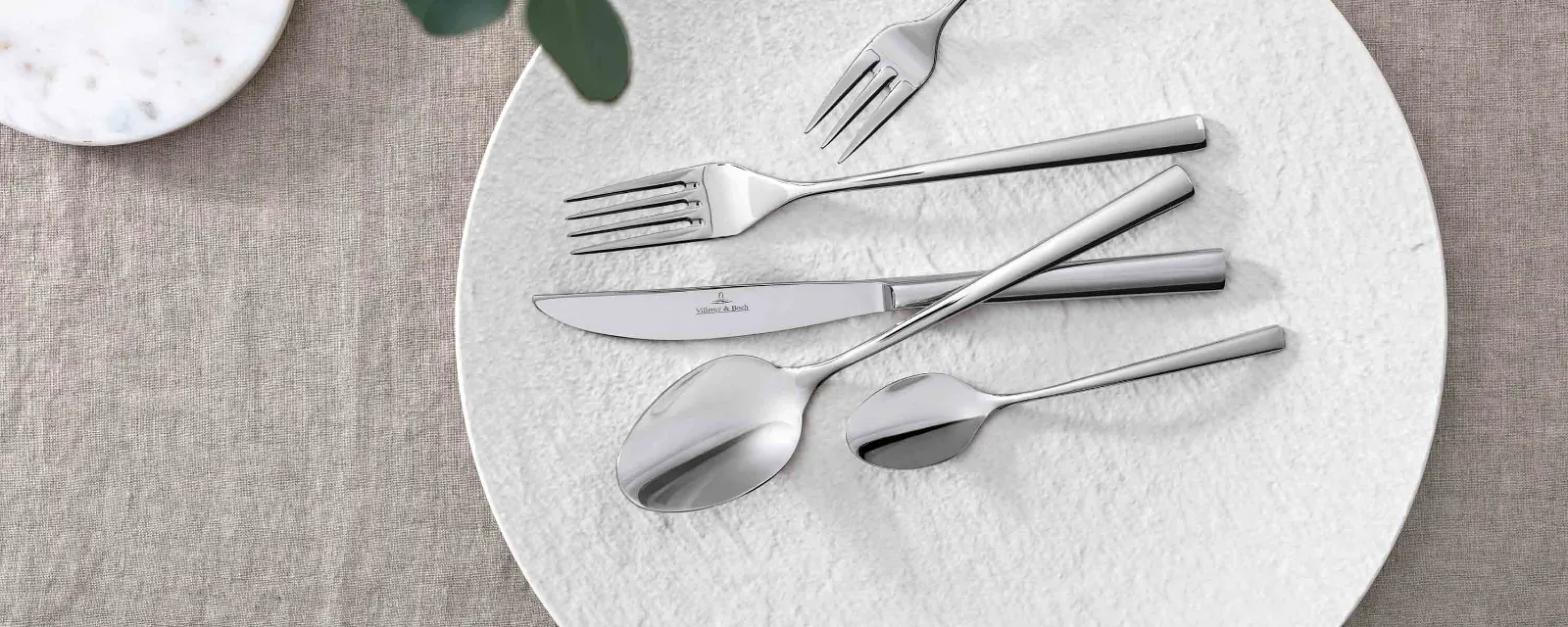 Elegant table decoration with modern Piemont cutlery and decorative greenery on a neutral tablecloth.